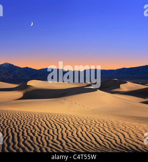 La lumière du soleil tôt le matin fusionne avec un crépuscule lune au-dessus des dunes de sable et des montagnes à Death Valley National Park, California, USA Banque D'Images