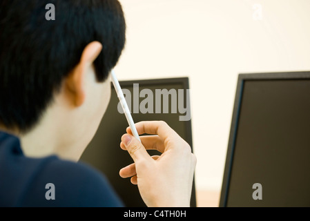 Jeune homme à la recherche de moniteurs d'ordinateur, holding de tête de la pensée contre crayon Banque D'Images