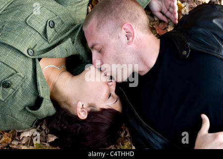 Un jeune couple s'embrasser passionnément tout en jetant dans certaines feuilles de l'automne. Banque D'Images