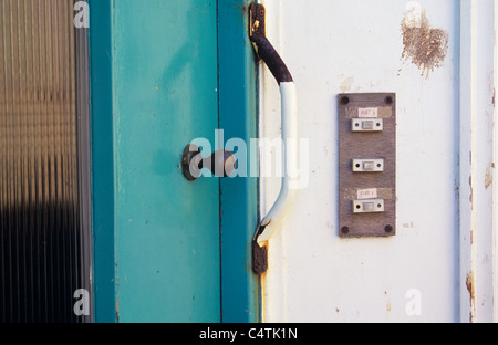 Entrée au bloc d'appartements délabrés avec trois boutons de sonnerie de porte avant turquoise poignée rouillée et chute d'oiseaux Banque D'Images