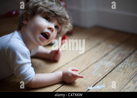 Toddler lying on floor avec cuillère à la main, pointant vers la nourriture renversée Banque D'Images