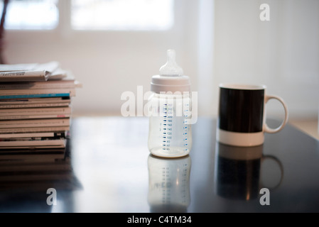 Biberon, tasse à café et pile de magazines Banque D'Images