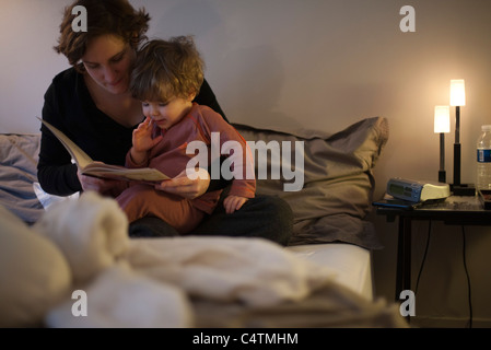 Mère tenant petit garçon sur les genoux, histoire de la lecture au lit Banque D'Images