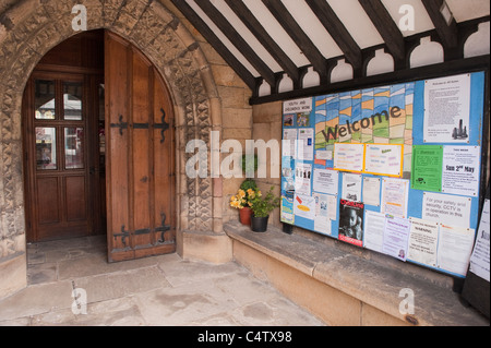 Intérieur porche de l'église (affiches épinglées sur le panneau d'affichage, portes en bois, porte, arche sculptée en pierre) - Eglise des Saints, Ilkley, Yorkshire, Angleterre, Royaume-Uni. Banque D'Images