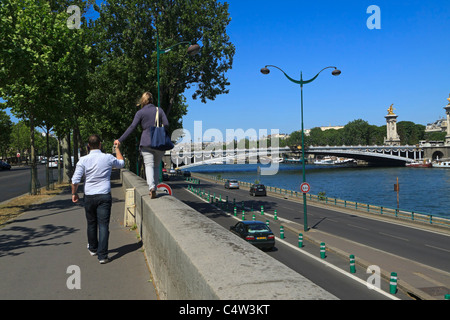 Sites touristiques de Paris. Un couple marche le long du quai d'Orsay à côté de la Seine vers le Pont Alexandre III. Banque D'Images