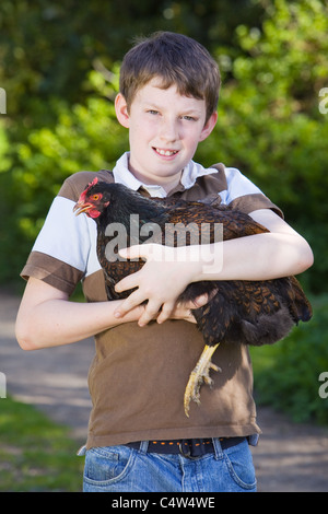 Un jeune garçon tenant un poulet brun foncé dans ses bras à l'extérieur par une journée ensoleillée Banque D'Images