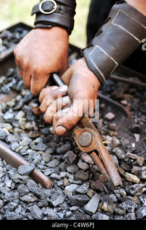 Détail de dirty hands holding pince - blacksmith Banque D'Images