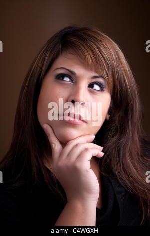 Une jolie jeune femme hispanique posant avec sa main sur son menton croit profondément à quelque chose sur son esprit. Banque D'Images