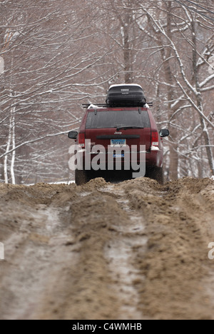 Une voiture fait son chemin le long d'une route boueuse pendant la saison de la boue dans le Vermont au printemps. Banque D'Images