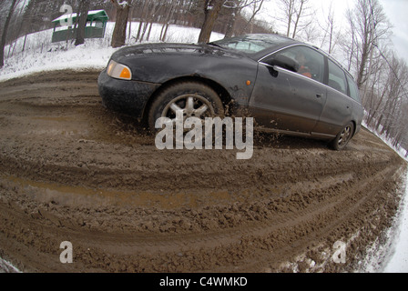 Une voiture fait son chemin le long d'une route boueuse pendant la saison de la boue dans le Vermont au printemps. Banque D'Images