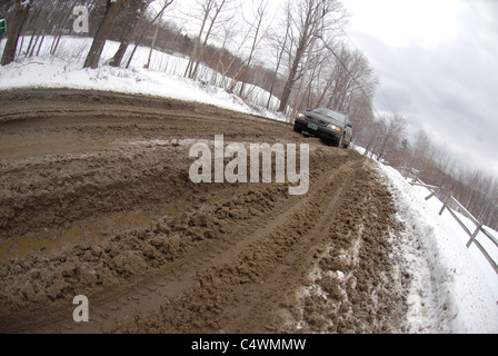 Une voiture fait son chemin le long d'une route boueuse pendant la saison de la boue dans le Vermont au printemps. Banque D'Images