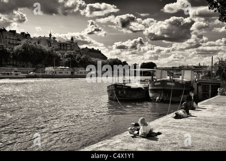 Image en noir et blanc du groupe de jeune adulte entre 20 touristes en vous relaxant au bord de Seine et les chalands avec art book sous ciel dramatique Banque D'Images