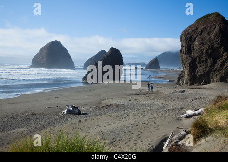 2 petites gens à pied sur la côte du Pacifique Grand Beach Oregon US large botte rocks petit couple tenir la main montagne ciel bleu nuages bas contexte Banque D'Images