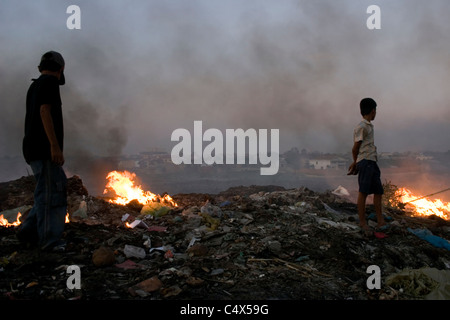 Deux enfants qui travaillent ont tendance les tas d'ordures qui brûlent dans un dépotoir toxique et polluée au Cambodge. Banque D'Images