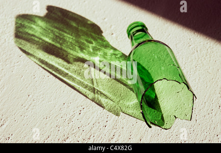 Flacon en verre vert brisé gisant sur sa surface blanche longue coulée d'ombre verte Banque D'Images