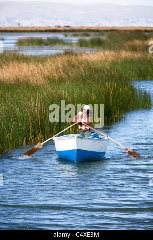 Une femme de lignes d'un bateau à travers les canaux de l'îles flottantes des Uros sur le lac Titicaca dans les Andes péruviennes. Banque D'Images