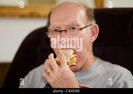 Un homme âgé mange un sandwich tout en restant assis dans un fauteuil. USA. Banque D'Images
