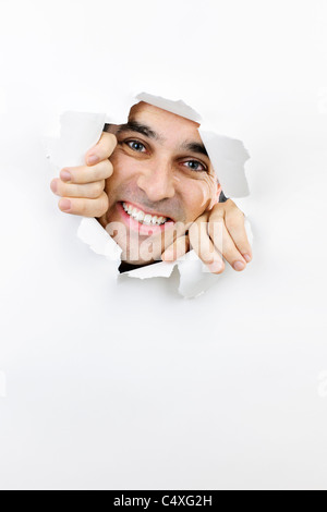 Papier déchiré dans le trou avec smiling man looking through Banque D'Images