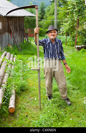 À l'aide de la faux agriculteur Senior tondre la pelouse traditionnellement Banque D'Images