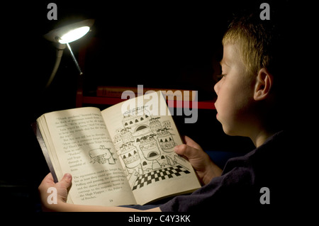 Réservez à l'heure du coucher un garçon de sept ans, la lecture d'un livre dans son lit à l'aide d'un jeune garçon,lampe,la famille qu'il prend de l'ingéniosité pour profiter de readi Banque D'Images