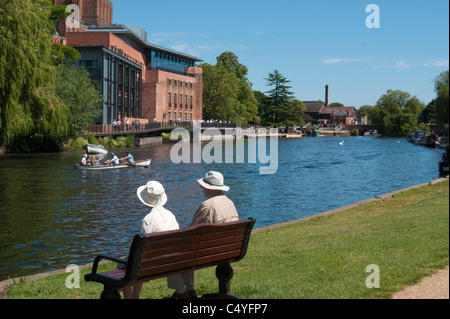 Un couple profiter du soleil au bord de la rivière Avon, à Stratford avec RSA theatre en arrière-plan. UK Banque D'Images