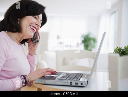 Mixed Race woman using laptop and talking on telephone Banque D'Images