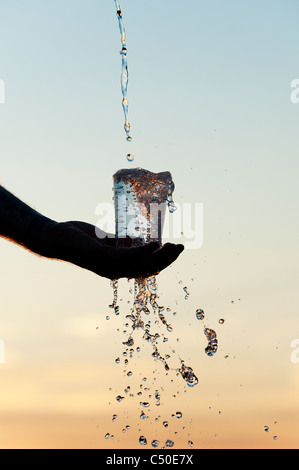 L'eau est versée dans une tasse en plastique au coucher du soleil. Silhouette. L'Inde Banque D'Images