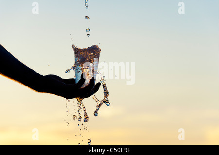 L'eau est versée dans une tasse en plastique au coucher du soleil. Silhouette. L'Inde Banque D'Images