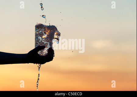 L'eau est versée dans une tasse en plastique au coucher du soleil. Silhouette. L'Inde Banque D'Images