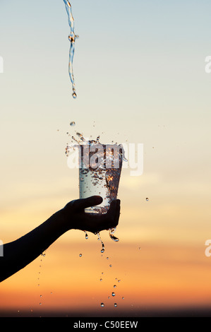 L'eau est versée dans une tasse en plastique au coucher du soleil. Silhouette. L'Inde Banque D'Images