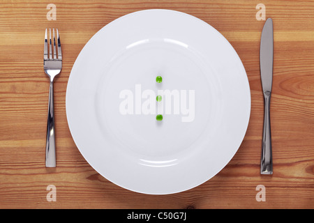 Photo de trois petits pois sur une plaque blanche avec fourchette et couteau sur une table en bois rustique. Banque D'Images