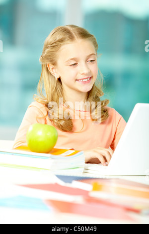 Portrait de l'écolière smart sitting in classroom et dactylographie Banque D'Images