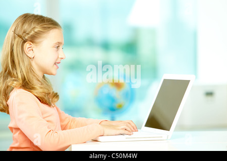 Portrait de l'écolière smart sitting in classroom et dactylographie Banque D'Images