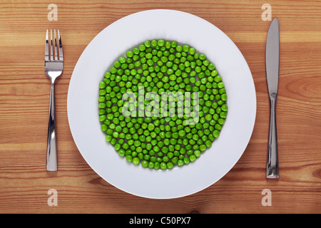 Photo de petits pois sur une plaque blanche avec fourchette et couteau sur une table en bois rustique. Banque D'Images