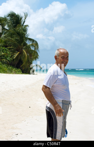 Une ancienne Hispanic Senior citizen homme debout sur une plage tropicale dans les Caraïbes. Banque D'Images