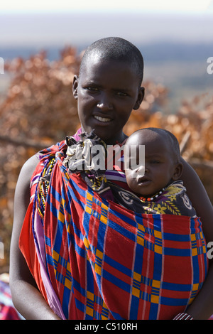 Close-up de jeunes Masaïs mère portant infant baby smiling enveloppée de rouge vif et bleu traditionnel couverture plaid Maasai Mara Kenya Afrique Banque D'Images