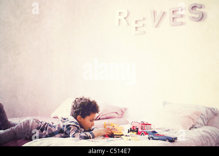 Little Boy lying on stomach on bed Playing with toy cars Banque D'Images