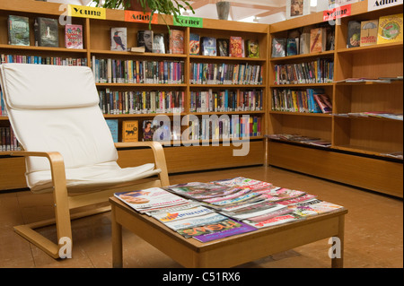 Vue rapprochée de l'intérieur de la bibliothèque de branche publique (livres de fiction pour jeunes adultes, étagères, magazines, table, chaise confortable) - Baildon, Yorkshire, Angleterre, Royaume-Uni Banque D'Images