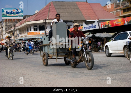 Un homme tire un wagon avec une moto tandis qu'un autre homme est maintenant la charge sur une rue de ville au Cambodge. Banque D'Images