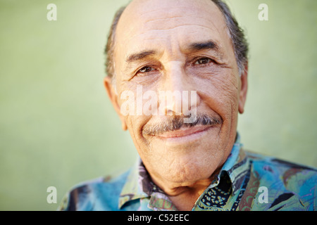 Portrait of senior hispanic man avec moustache looking at camera contre mur vert et souriants. De forme horizontale, copy space Banque D'Images