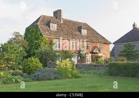 Pigeonnier cottage, tôt le matin, brique avec toit de tuiles en pierre de Cotswold fleurs rouge vert Banque D'Images