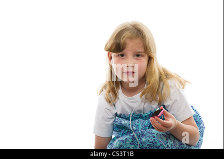 Une jeune fille de 7 ou 8 ans l'écoute d'un ipod/mp3 player sur un fond blanc studio arrière-plan. Banque D'Images