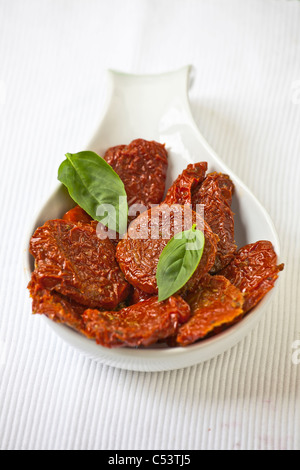Plusieurs tranches de tomates séchées dans un seau blanc avec des feuilles de basilic Banque D'Images