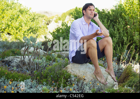 Mid adult man sitting on a rock and talking on a mobile phone Banque D'Images
