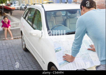 Vue arrière d'un homme regardant la carte sur voiture avec jeune femme assise à l'arrière-plan Banque D'Images