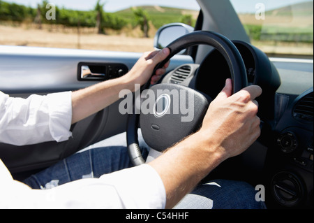 Mid adult man's hand holding un volant de voiture décapotable Banque D'Images