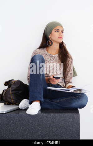 Belle femme à la voiture avec un téléphone mobile et livre à la main contre fond blanc Banque D'Images