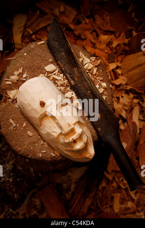 Un masque en bois sculpté avec vintage machette dans l'avant-plan et les copeaux de bois en arrière-plan. Banque D'Images