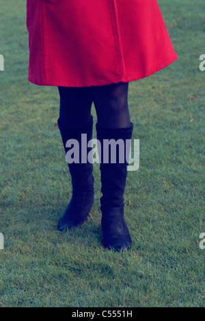 Femme en bottes noires et red coat walking on grass Banque D'Images