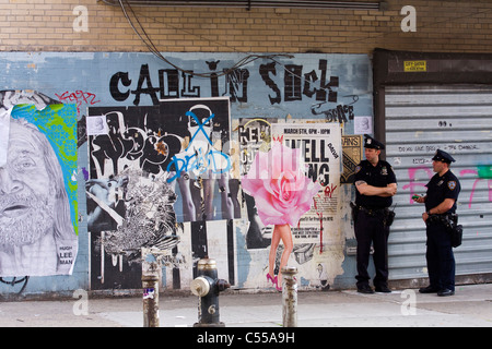 Les agents de police de patrouiller à pied sur le trottoir à côté d'un graffiti sur un mur de brique dans le West Village de New York. Banque D'Images